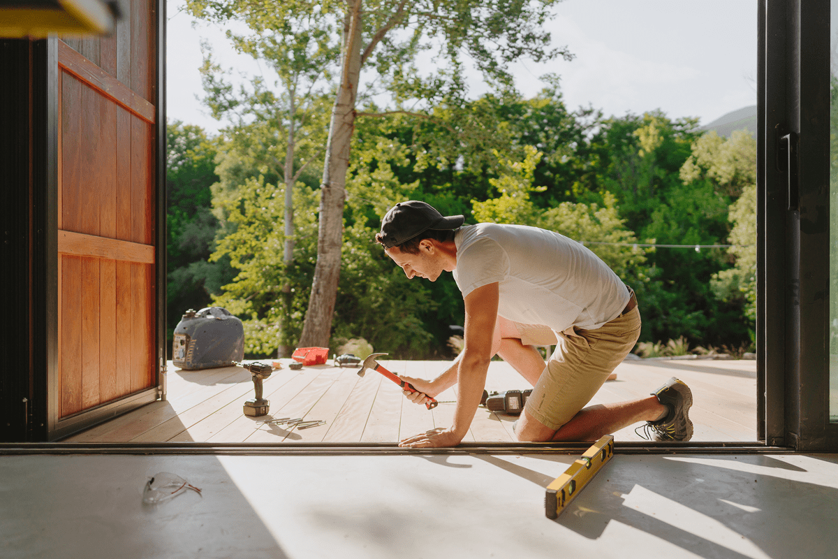 Person hammering nails on wooden deck outside.
