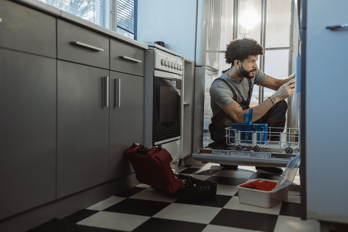 Man repairing dishwasher in modern kitchen.