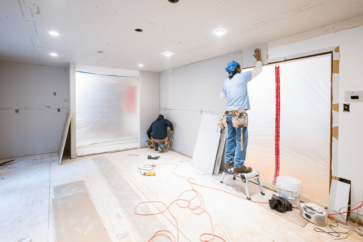 Workers installing drywall in a room.