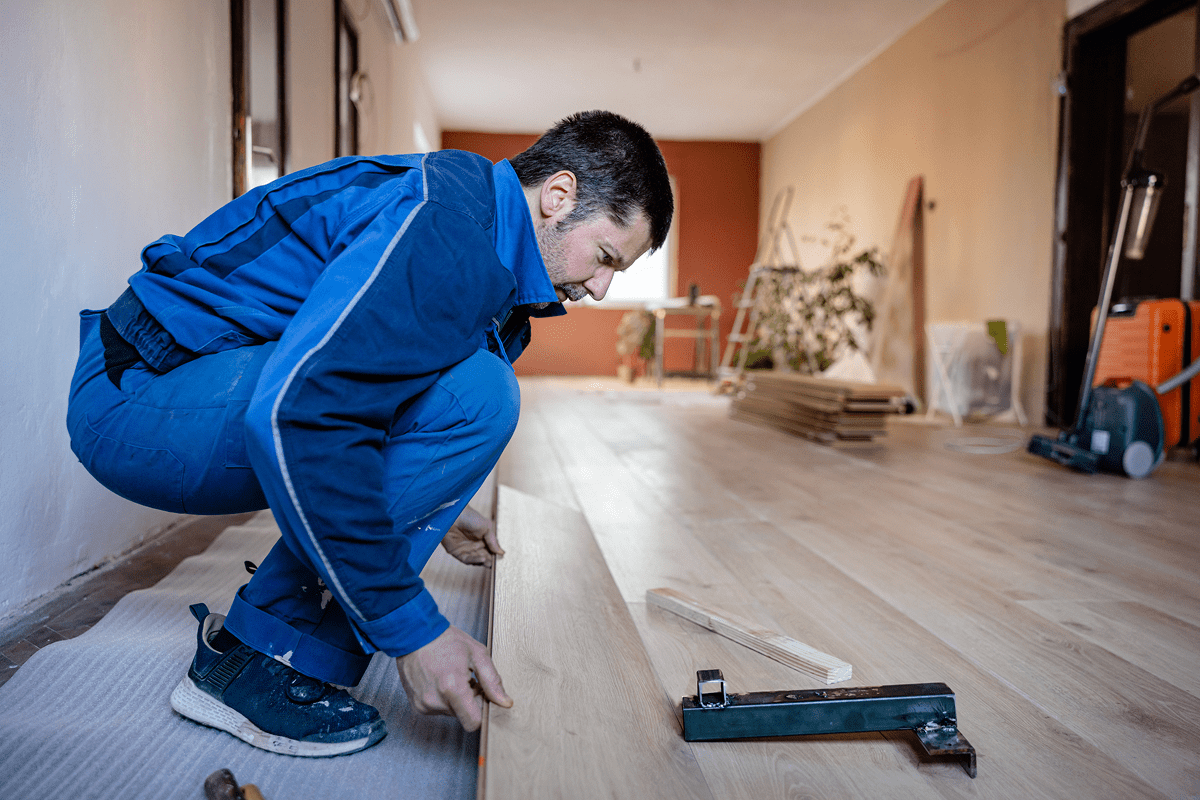 Man installing laminate flooring in room.